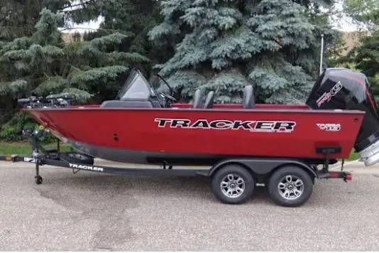 Slide: The Image of 2026 Tracker Targa V-19 Combo boat on trailer, red exterior, parked near trees. - 10