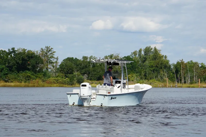 Slide: The Image of 2023 Maycraft 2100 CC boat cruising on a calm lake with lush green shoreline. - 6
