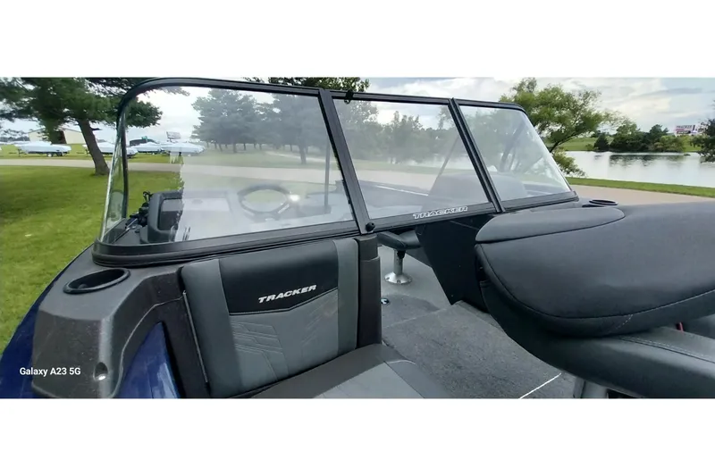 Slide: The Image of 2024 Tracker Targa V-18 Combo boat interior with windshield and seating, near a scenic lake. - 23