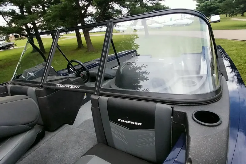 Slide: The Image of 2024 Tracker Targa V-18 Combo boat interior with windshield and seating, parked near trees. - 32
