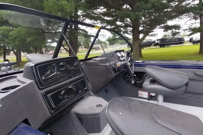 Slide: The Image of 2024 Tracker Targa V-18 Combo boat interior with seating and dashboard, surrounded by trees. - 38