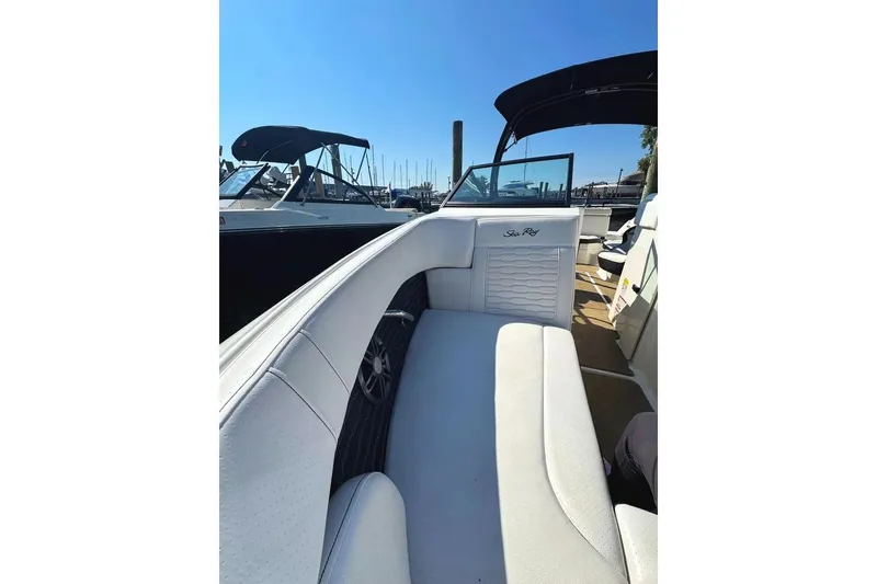 Slide: The Image of 2022 Sea Ray SPX 230 Outboard boat interior with white seating and marina background. - 12
