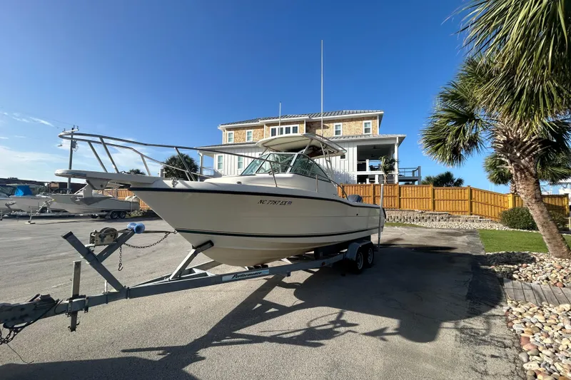 Slide: The Image of 2000 Pursuit 2470 Walkaround boat on trailer, parked near a coastal house. - 3