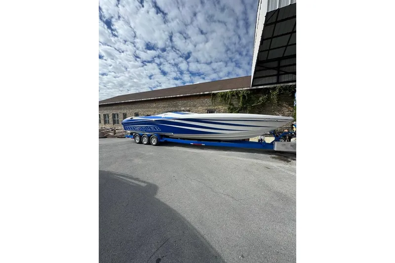 Slide: The Image of 2016 Hustler 39 boat on trailer, blue and white design, parked outdoors under cloudy sky. - 1