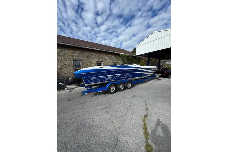 Slide: The Image of 2016 Hustler 39 boat on trailer, blue and white design, parked outdoors. - 3