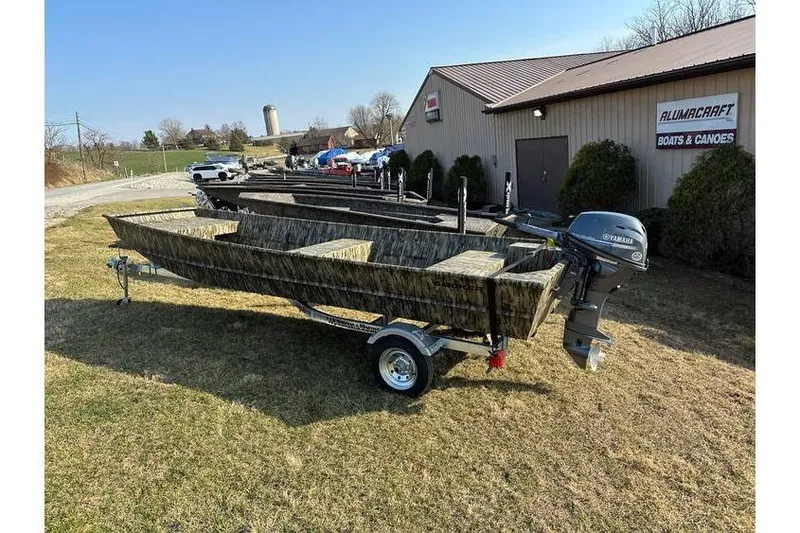 Slide: The Image of 2025 Smoker Craft 1648 Jon boat on trailer, parked outside Alumacraft dealership. - 3