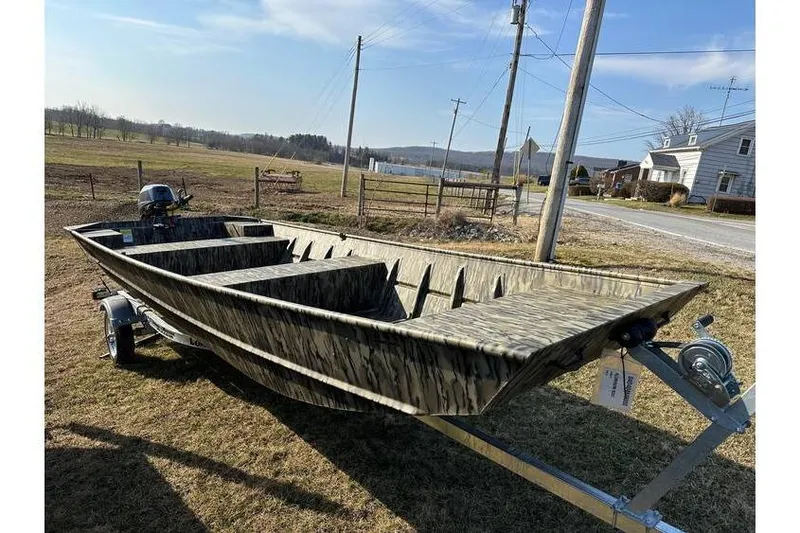 Slide: The Image of 2025 Smoker Craft 1648 Jon boat on trailer, camo design, parked in rural setting. - 6