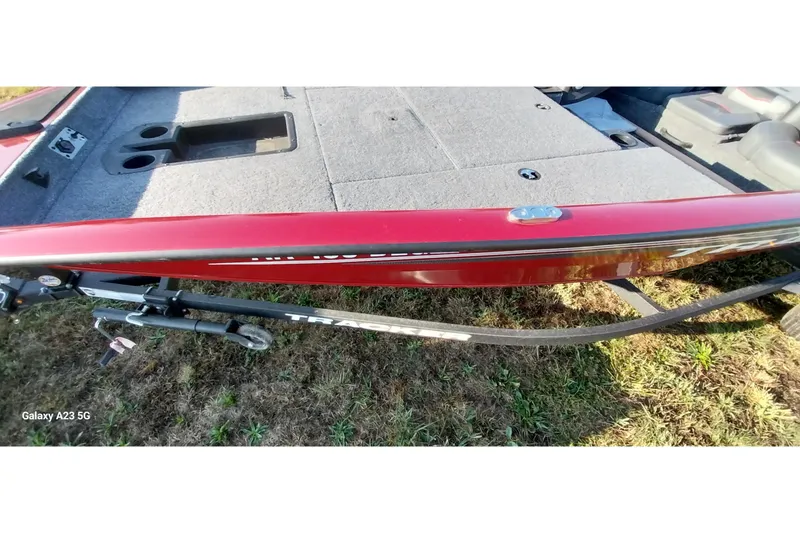 Slide: The Image of 2024 Tracker Pro Team 175 TXW boat, red exterior, carpeted deck, on grassy ground. - 18