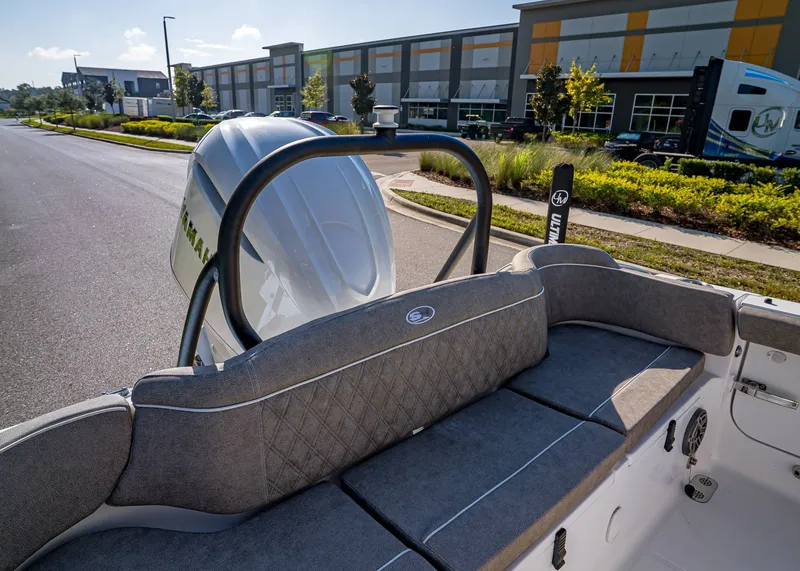 Slide: The Image of 2026 Sea Hunt Ultra 255 SE boat with cushioned seating, parked near modern buildings. - 15