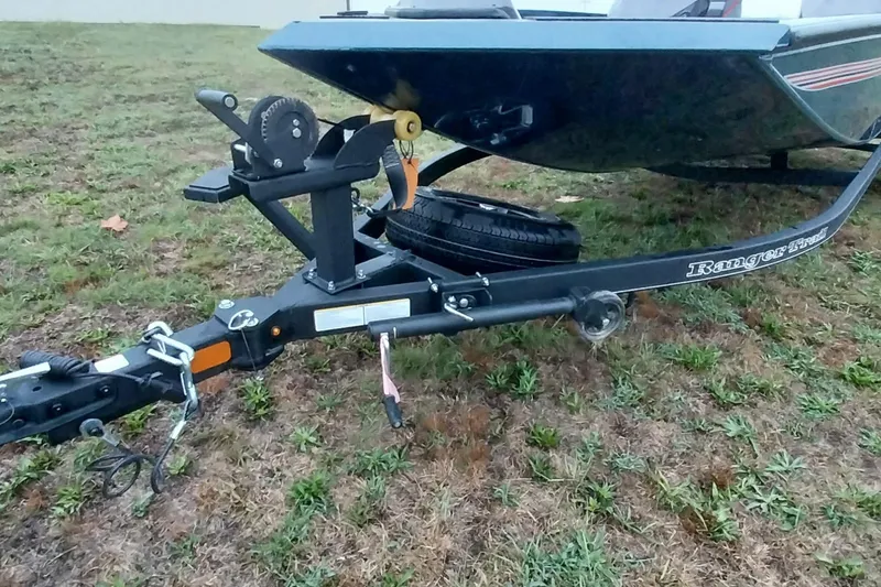 Slide: The Image of 2024 Ranger RT198P boat trailer on grassy terrain, featuring a spare tire and hitch. - 39