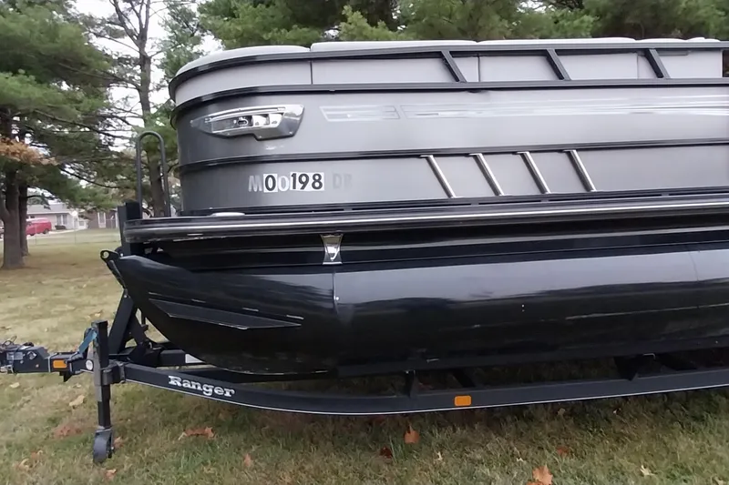 Slide: The Image of 2020 Ranger 2500LS pontoon boat on trailer, parked on grass with trees in background. - 25