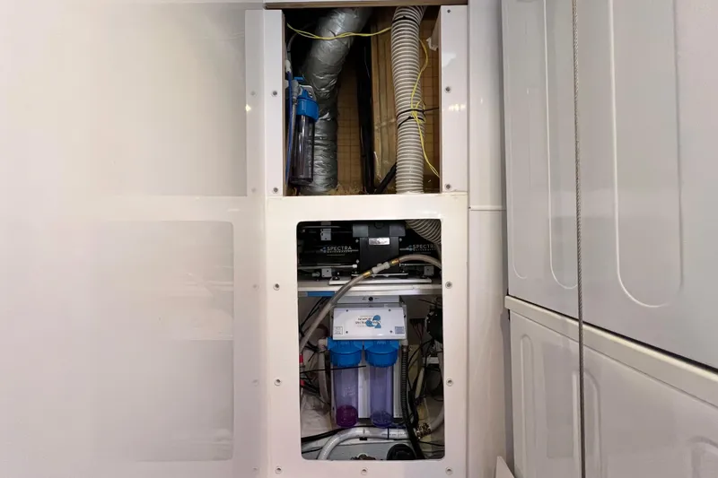 Slide: The Image of Laundry area with stacked washer-dryer in 2019 Aquila 44 yacht, featuring wooden flooring and compact sink. - 98