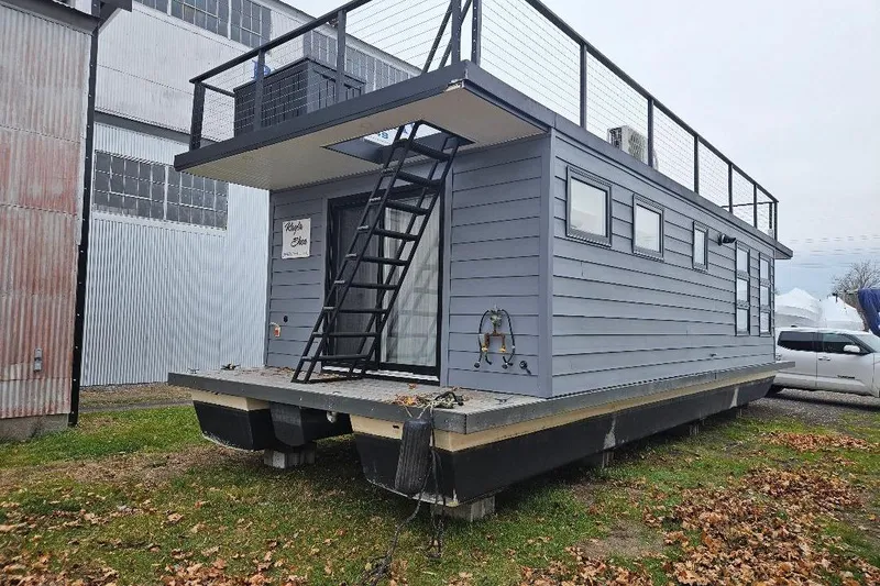 Slide: The Image of 2021 East Coast Houseboats Freedom 40, modern design, docked on grass near industrial building. - 22