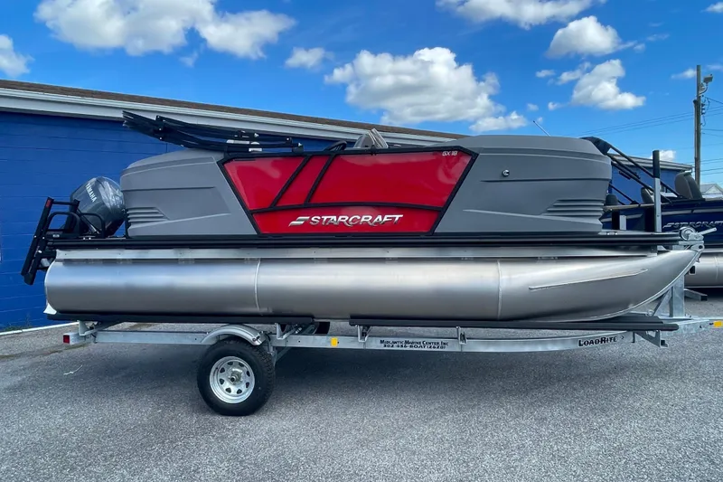 The Image of 2026 Starcraft GX 18 R pontoon boat on trailer, red and gray design, parked outdoors. - 0