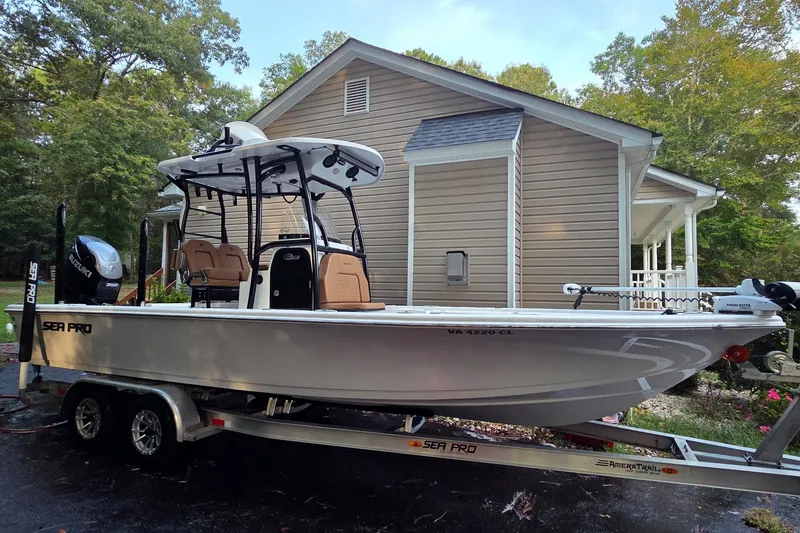 Slide: The Image of 2024 Sea Pro 250 Bay boat on trailer, parked near a house with trees in the background. - 15