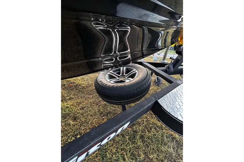 Slide: The Image of 2024 Triton 179 TrX boat trailer with spare tire on grassy ground. - 1
