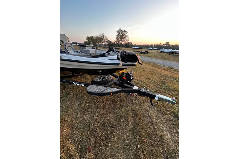 Slide: The Image of 2024 Triton 179 TrX boat on trailer at sunset, parked on grassy field. - 24