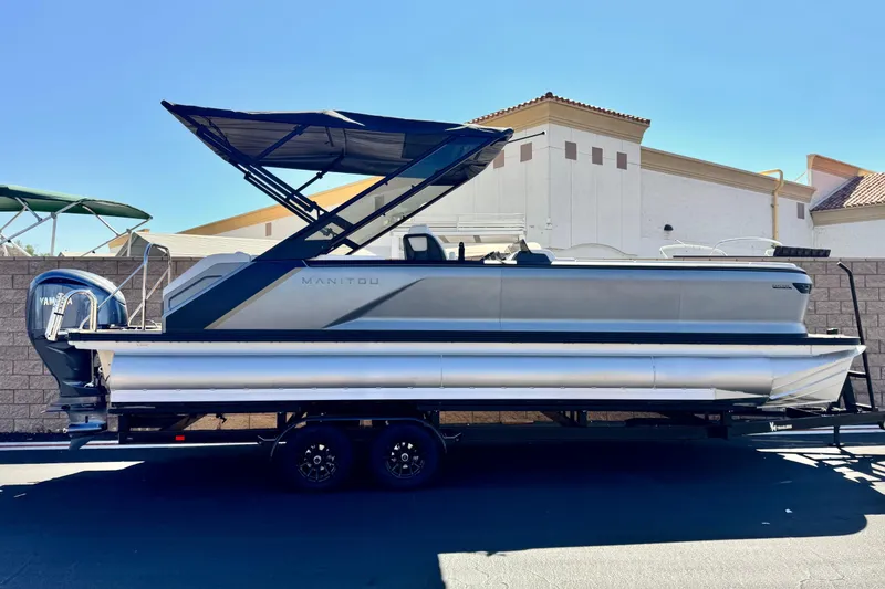 The Image of 2025 Manitou EXPLORE 26 pontoon boat on trailer, side view, with Yamaha engine. - 0