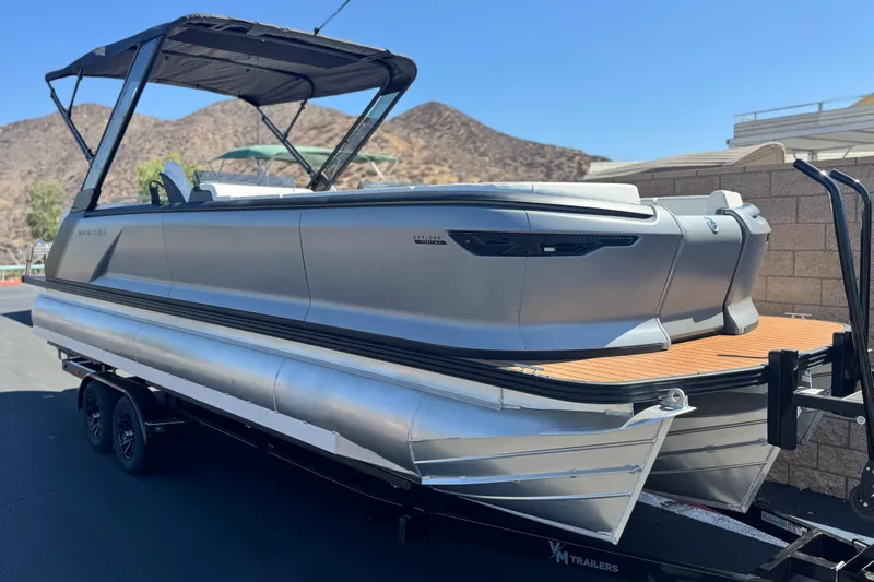 Slide: The Image of 2025 Manitou EXPLORE 26 pontoon boat on trailer, sleek design, mountainous background. - 1