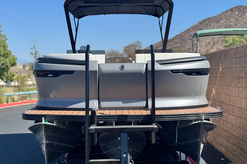 Slide: The Image of 2025 Manitou EXPLORE 26 pontoon boat, rear view, parked outdoors with scenic background. - 2