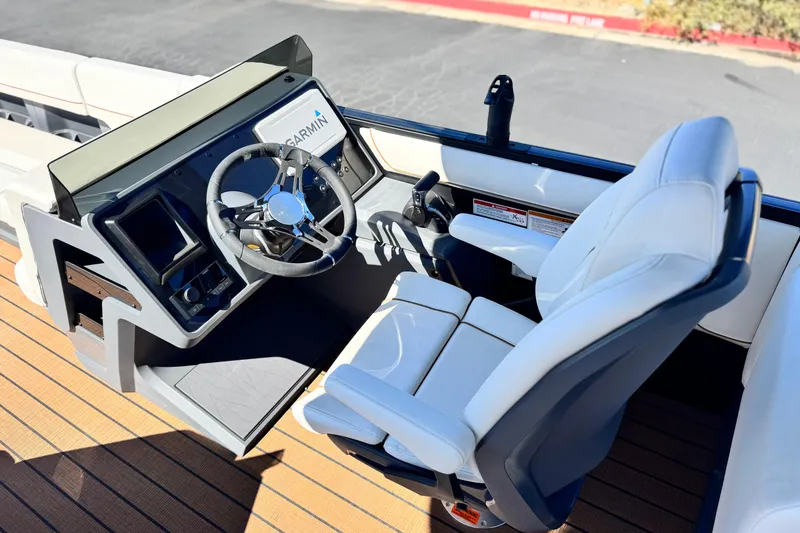 Slide: The Image of 2025 Manitou EXPLORE 26 boat cockpit with steering wheel, Garmin display, and white captain's chair. - 24