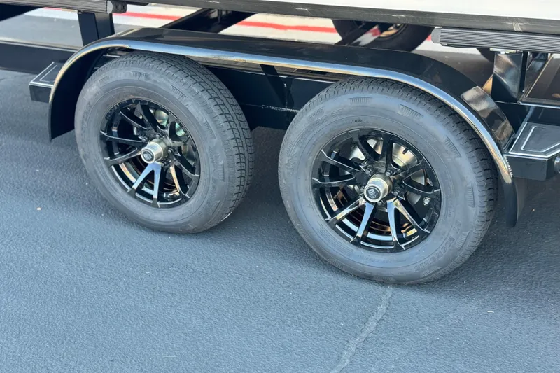 Slide: The Image of 2025 Manitou EXPLORE 26 trailer wheels, black rims on asphalt surface. - 26