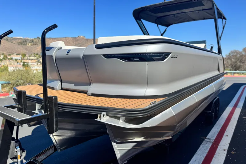 Slide: The Image of 2025 Manitou EXPLORE 26 pontoon boat on trailer, sleek design, outdoor setting. - 3