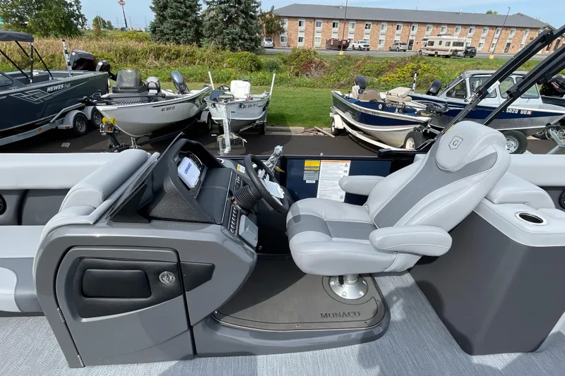 Slide: The Image of Captain's seat and helm of 2026 Godfrey Monaco 235 SB pontoon boat, surrounded by other boats. - 15