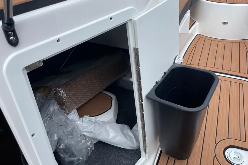 Slide: The Image of 2026 Yamaha 222SE boat storage compartment with open door and black trash bin. - 16