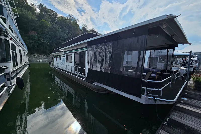 The Image of 1985 Sumerset 14x60 houseboat docked on a calm lake with trees in the background. - 0