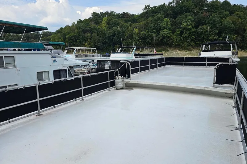 Slide: The Image of 1985 Sumerset 14x60 houseboat with spacious deck, docked near lush green shoreline. - 27