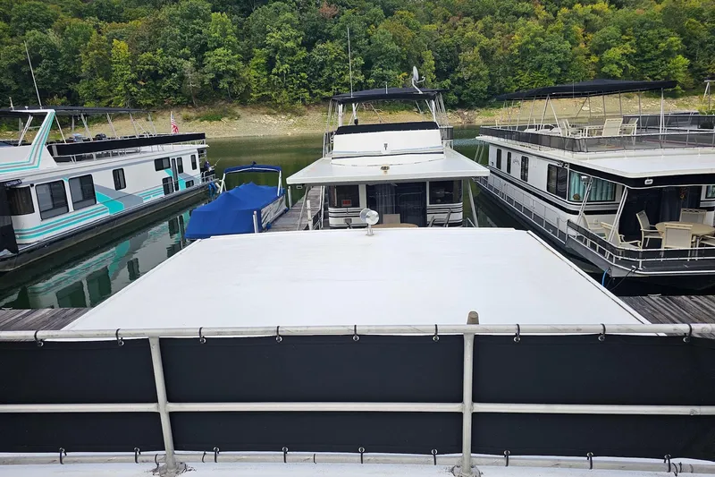 Slide: The Image of Houseboats docked on a calm lake, surrounded by lush green trees, featuring a 1985 Sumerset 14x60. - 28