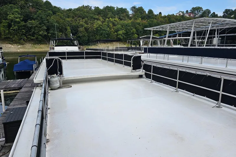 Slide: The Image of 1985 Sumerset 14x60 houseboat with spacious deck, docked near lush green shoreline. - 30