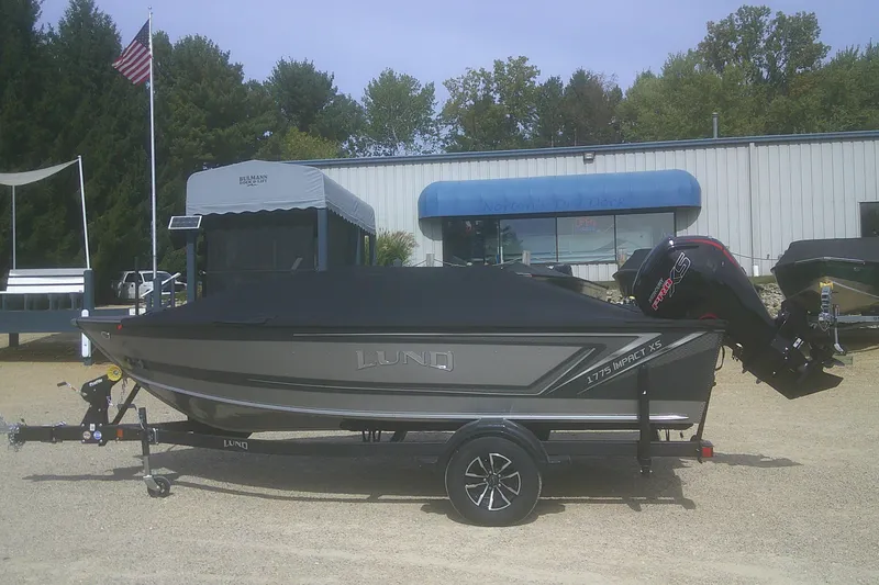 Slide: The Image of 2026 Lund 1775 Impact XS SS boat on trailer, covered, with outboard motor. - 13