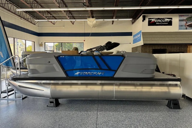 Slide: The Image of 2026 Starcraft GX 18 R pontoon boat displayed in showroom, featuring sleek blue and gray design. - 1
