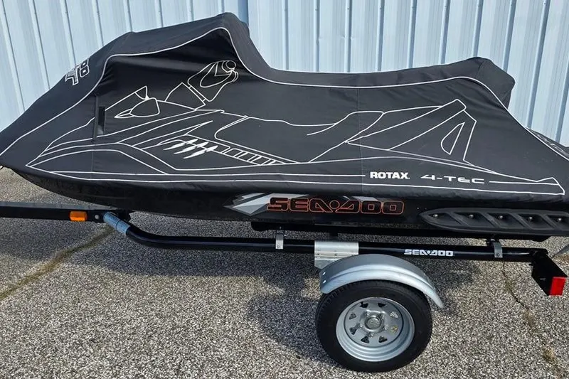 Slide: The Image of 2009 Sea-Doo RXT 255 jet ski covered on trailer, parked on pavement. - 2