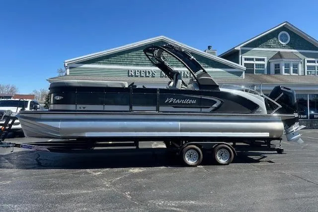 Slide: The Image of 2024 Manitou LX 25 SRS pontoon boat on trailer, parked outside a building. - 3