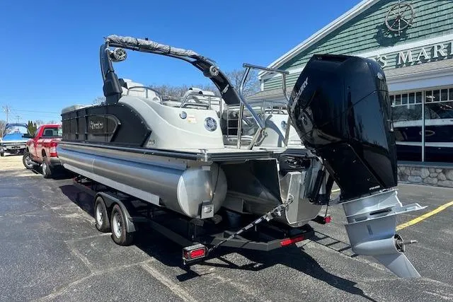 Slide: The Image of 2024 Manitou LX 25 SRS pontoon boat with powerful outboard motor, parked on trailer. - 5