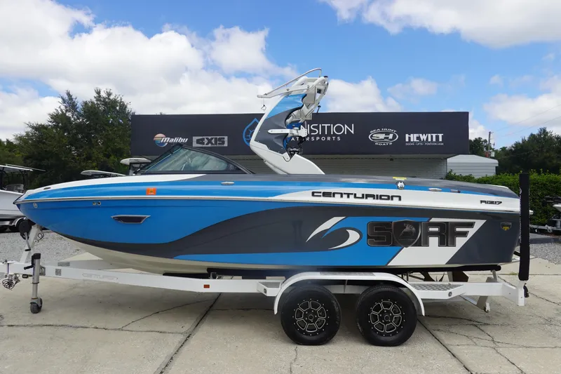The Image of 2017 Centurion Ri217 blue surf boat on trailer at dealership. - 1