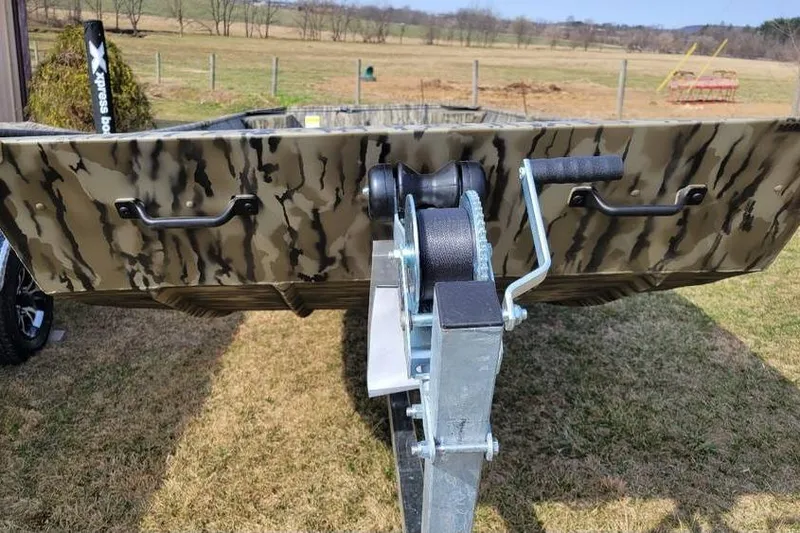 Slide: The Image of 2025 Smoker Craft 1648 jon boat with camo design on trailer in grassy field. - 3