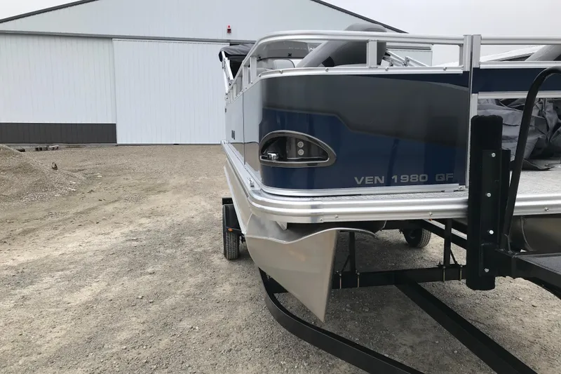 Slide: The Image of 2026 Avalon 19 Venture Quad Fish boat on trailer, parked near a large building. - 3