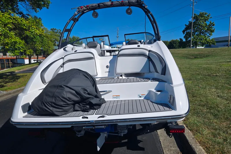 Slide: The Image of 2018 Yamaha Boats AR240, rear view, parked on grass, showcasing spacious deck and seating. - 2