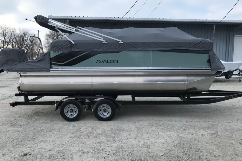The Image of 2026 Avalon Venture Quad Lounger 19' pontoon boat on trailer, covered and parked outdoors. - 0