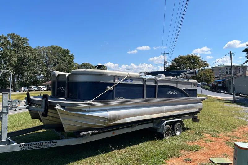 Slide: The Image of 2020 Manitou 23 Aurora LE Standard pontoon boat on trailer, parked on grass. - 1