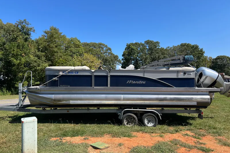 Slide: The Image of 2020 Manitou 23 Aurora LE Standard pontoon boat on trailer, parked on grass. - 2