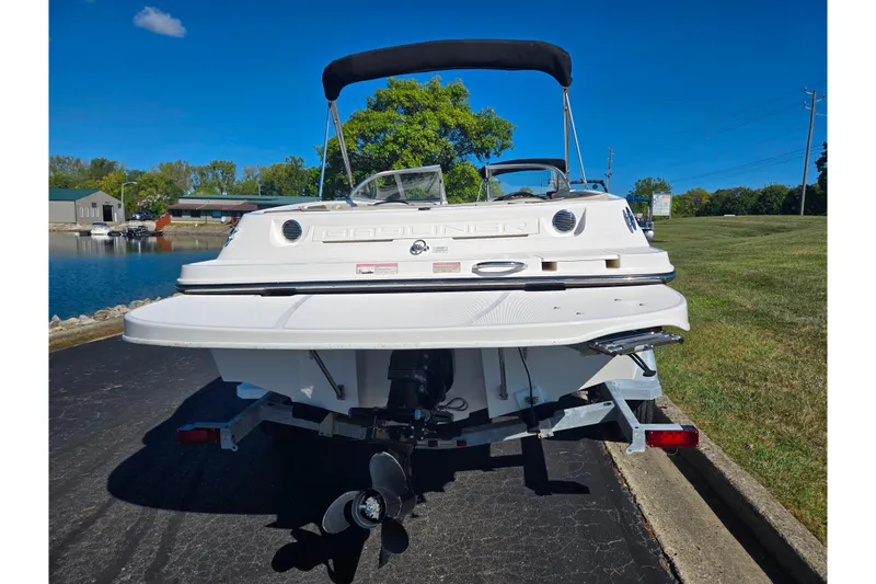 Slide: The Image of 2015 Bayliner 185 Bowrider boat on trailer, parked near a lake under clear blue sky. - 2