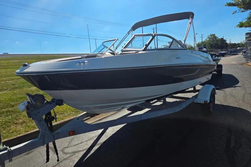 Slide: The Image of 2015 Bayliner 185 Bowrider on trailer, parked outdoors under clear blue sky. - 5