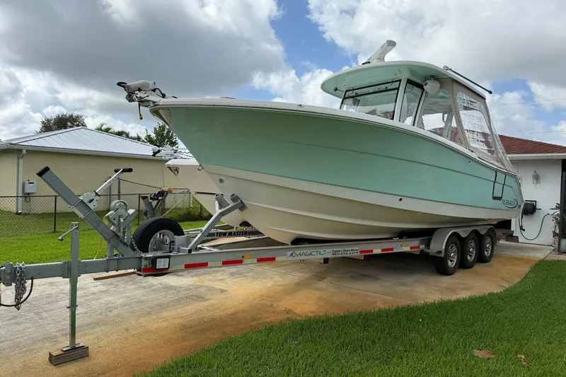 Slide: The Image of 2019 Robalo R300 Center Console boat on trailer, parked in driveway. - 0