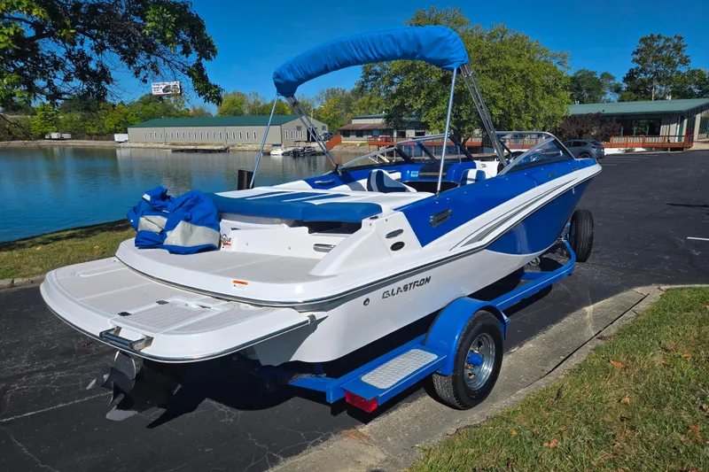 Slide: The Image of 2013 Glastron GT 205 boat with blue accents, parked near a serene lake. - 1
