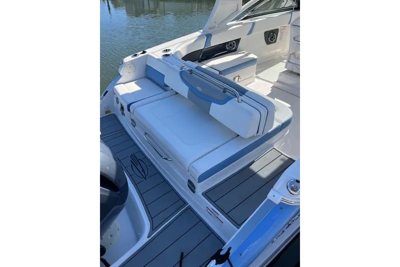 Slide: The Image of 2023 Chaparral 280 OSX boat interior with white and blue seating, docked by water. - 2